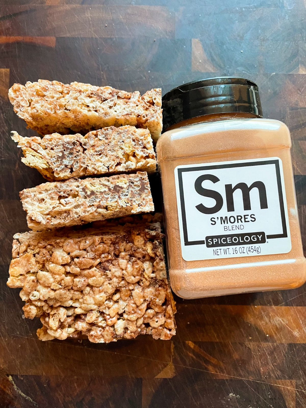 S’mores Rice Krispy treats stacked beside a jar of Spiceology S’mores Blend on a wooden surface