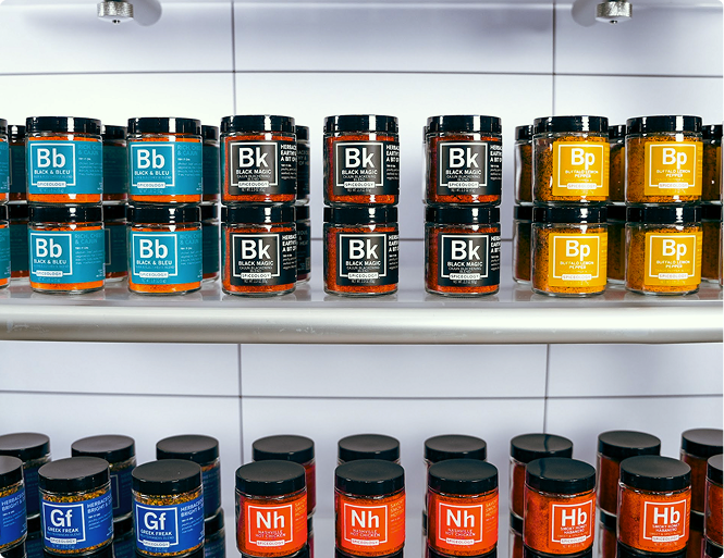 Multiple rows of colorful Spiceology spice blend jars arranged across two tiers of retail shelving, showcasing a wide variety of blends