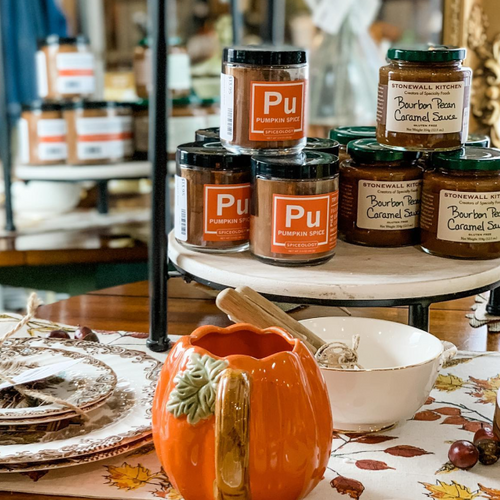 Spiceology Pumpkin Spice blend jars arranged on tiered shelves with a pumpkin decoration in the foreground, evoking a seasonal retail display