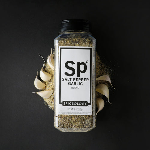 Spiceology Salt Pepper Garlic blend bottle on a dark background with garlic, flat-lay style