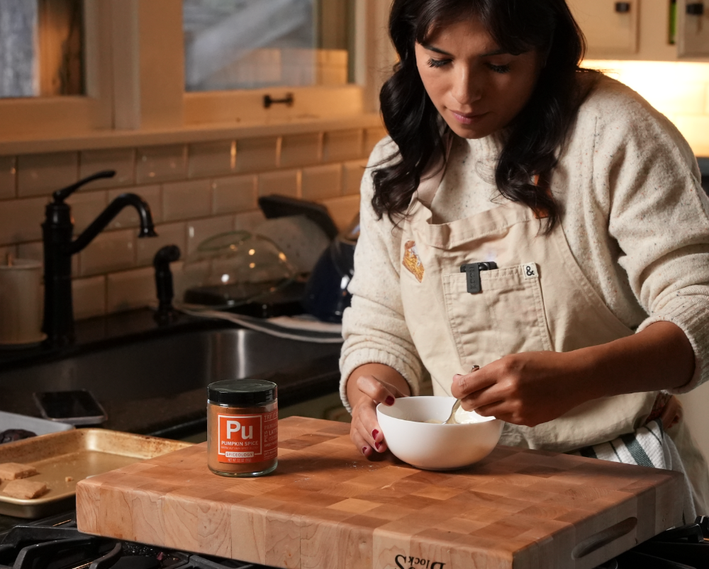 A person seasoning food in a small bowl on a wooden cutting board in a home kitchen