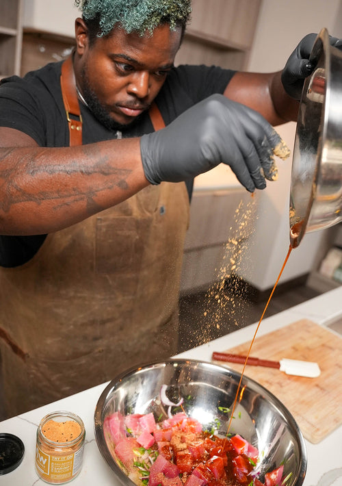 A chef wearing gloves working with ingredients in a stainless steel mixing bowl