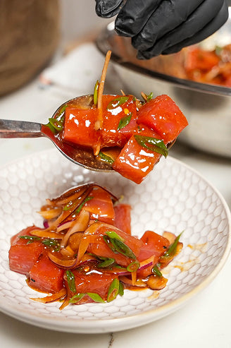 A gloved hand holding tongs with a saucy red protein on a white plate