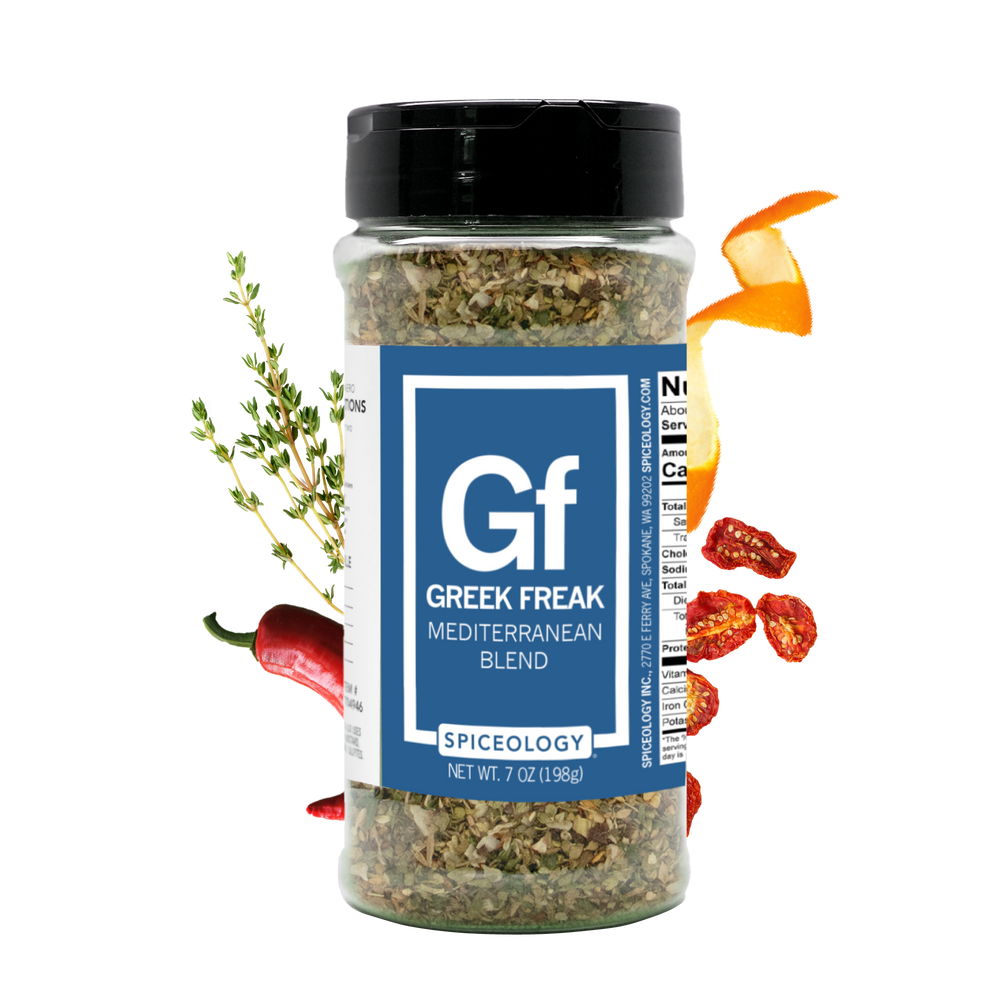 Spiceology Greek Freak blend large jar on black background with fresh herbs and spices arranged nearby