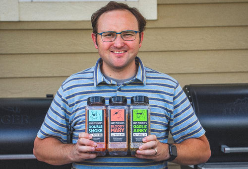 A man with glasses in a striped shirt smiling while holding multiple Spiceology blend jars