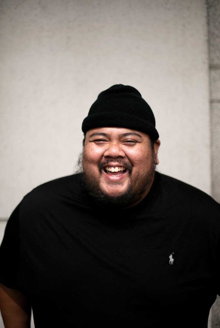 Portrait of a smiling man wearing a black beanie and black shirt against a light background