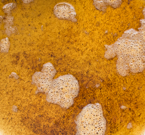 Close-up overhead view of golden yellow liquid showing groups of bubbles