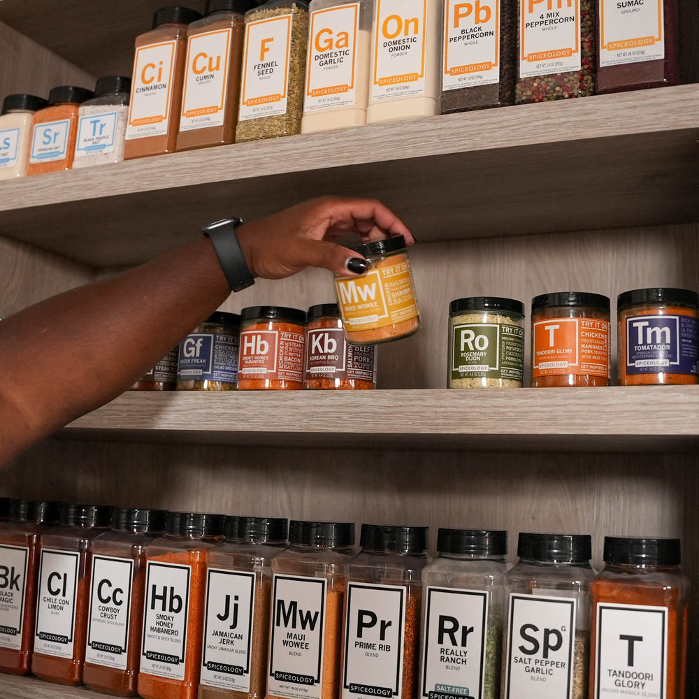 Wooden wall-mounted spice rack organizer with labeled glass jars displaying colorful cooking spices